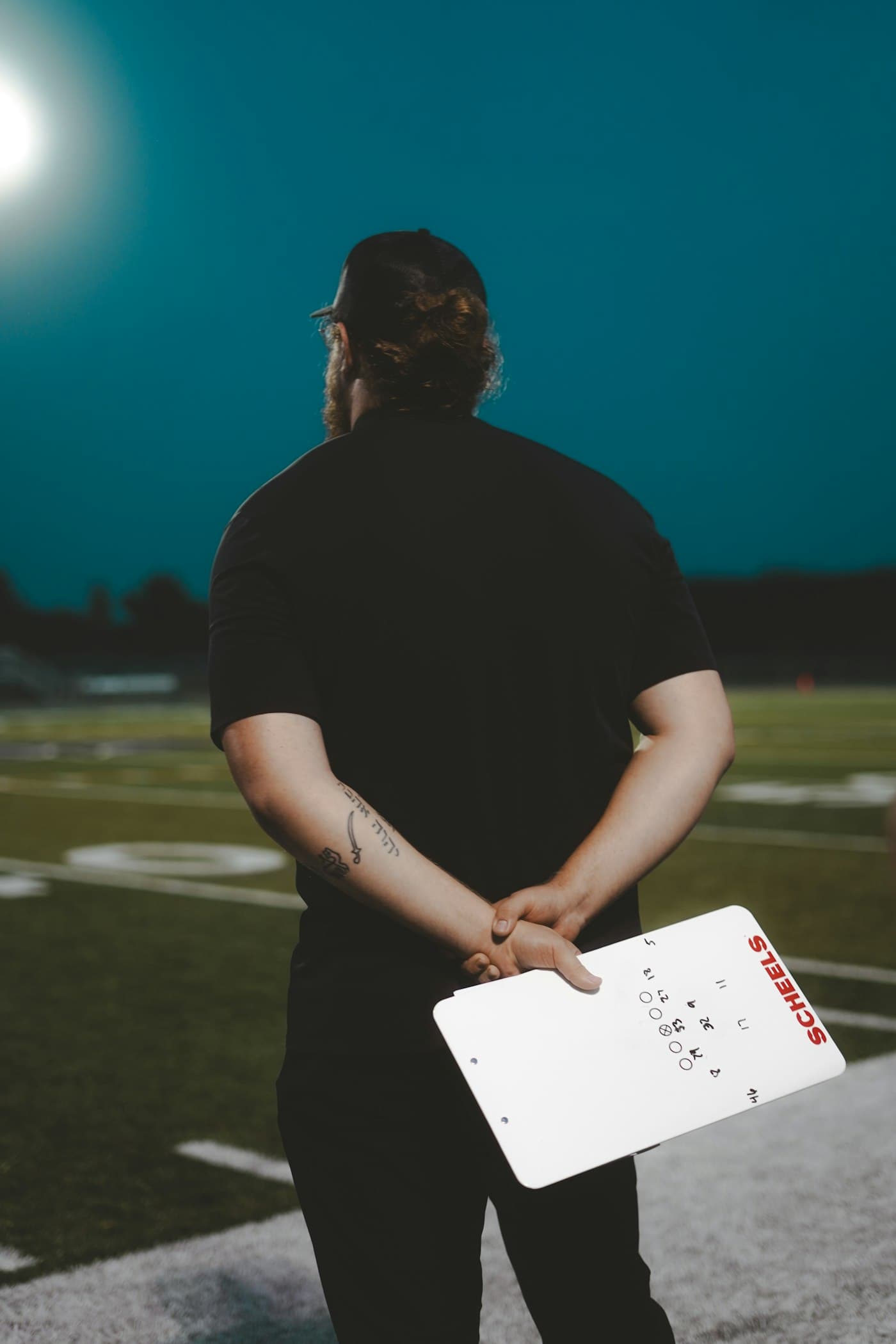 A football coach studying the field at dusk, call sheet in hand